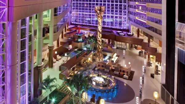 A multi-level hotel lobby featuring soft purple lighting, large windows, and a circular bar.
